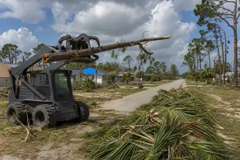 Sorted storm-fallen branches beside a reopened driveway under clearing Southwest Florida skies